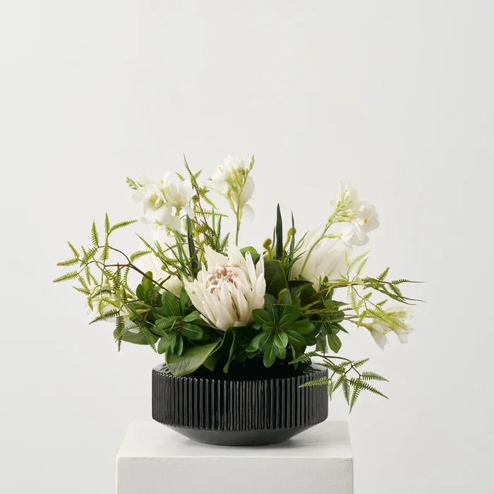 Jungle Elegance – Large White Protea Blooms, Wild Fern & Pittosporum Tropical everyday Modern Floral Arrangement in Rounded Black Glass Vase